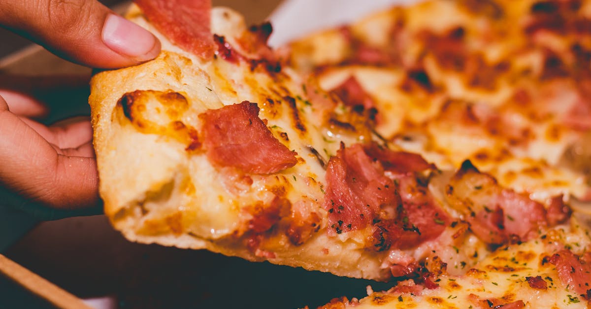 Close-up of a hand holding a delicious slice of pepperoni pizza.
